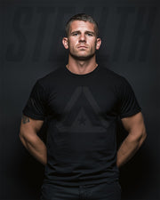Man wearing a black t-shirt with a logo on a dark background