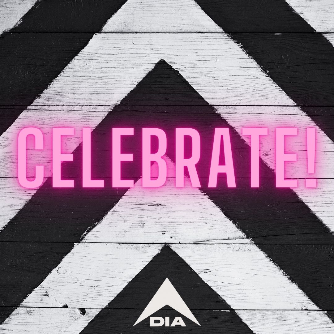 Pink neon "CELEBRATE!" text centered over a black and white chevron wood background with a small white DIA logo at the bottom