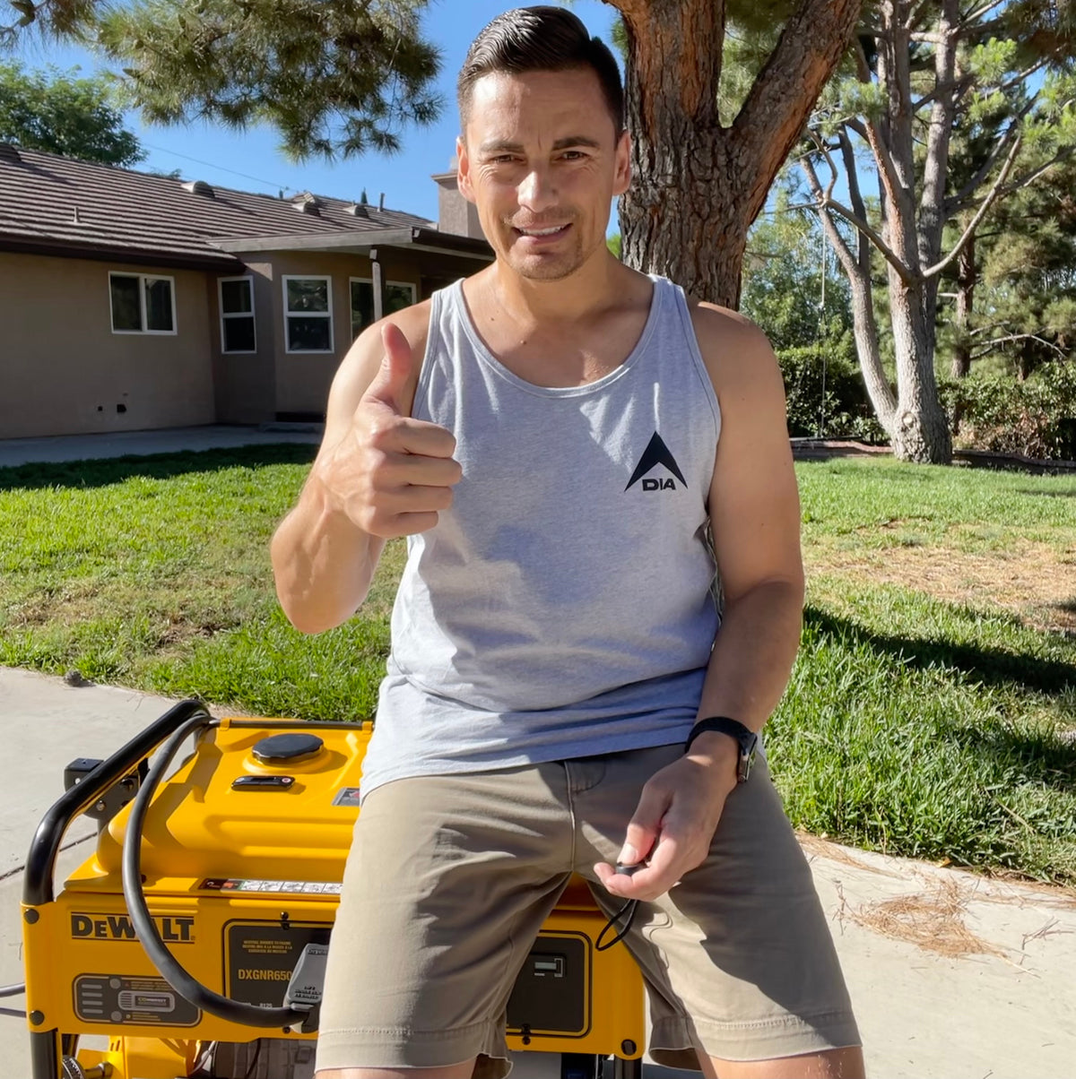 Man outdoors giving a thumbs up, sitting on a yellow DeWalt generator, wearing a light gray tank top with a DIA logo.