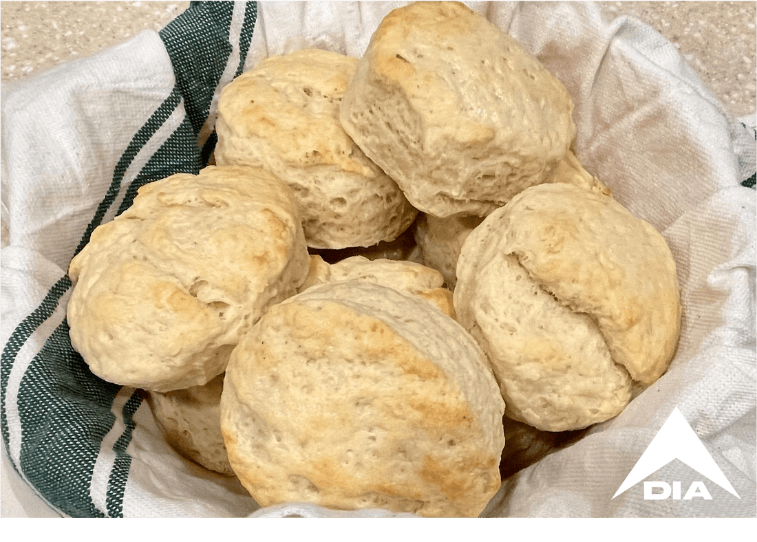 Basket of golden-brown biscuits on a green-striped towel in a kitchen, featuring a white DIA logo in the corner.