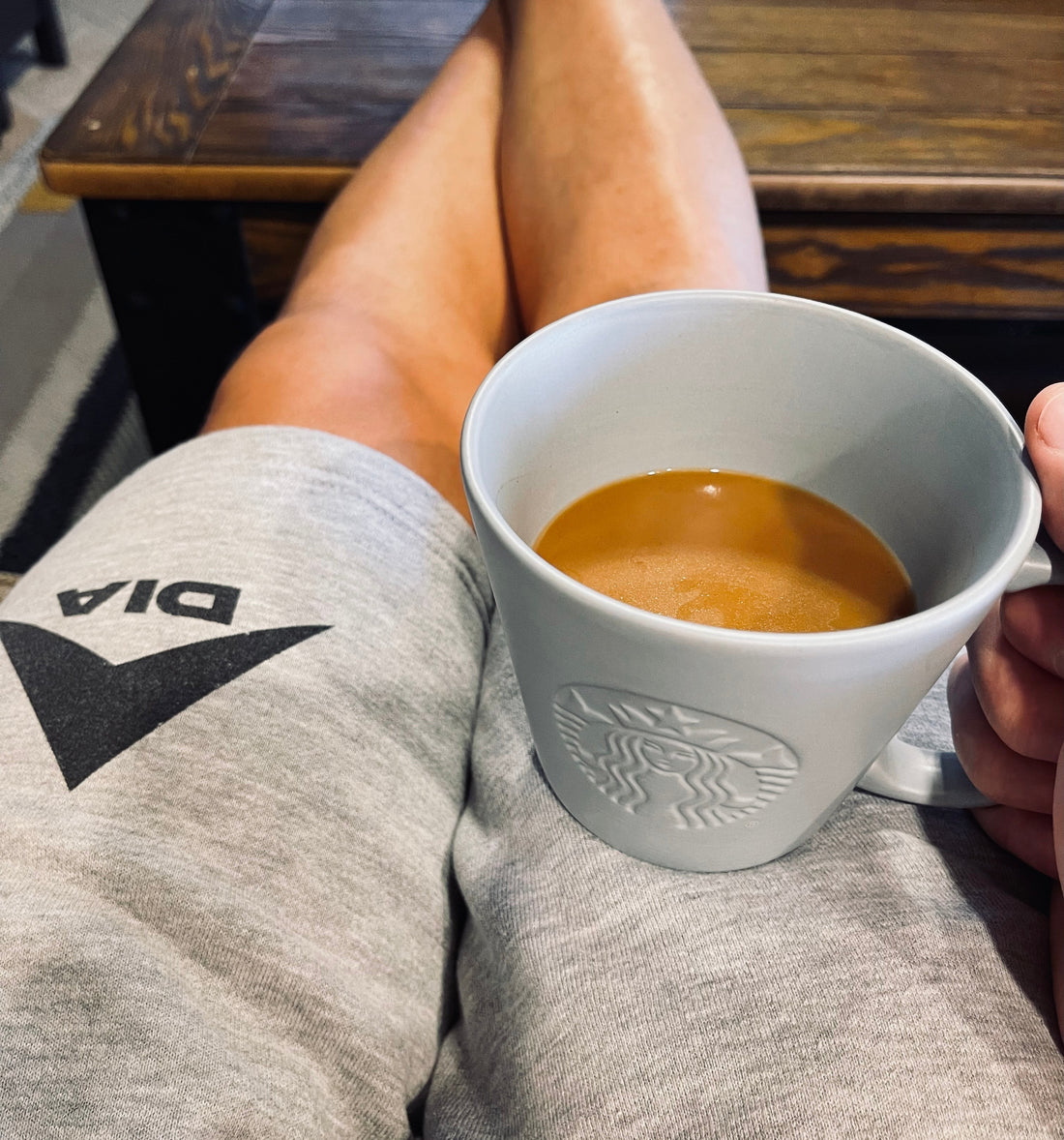 Person with crossed legs, indoor setting with a table, with gray DIA sweatpants and a white Starbucks coffee mug.