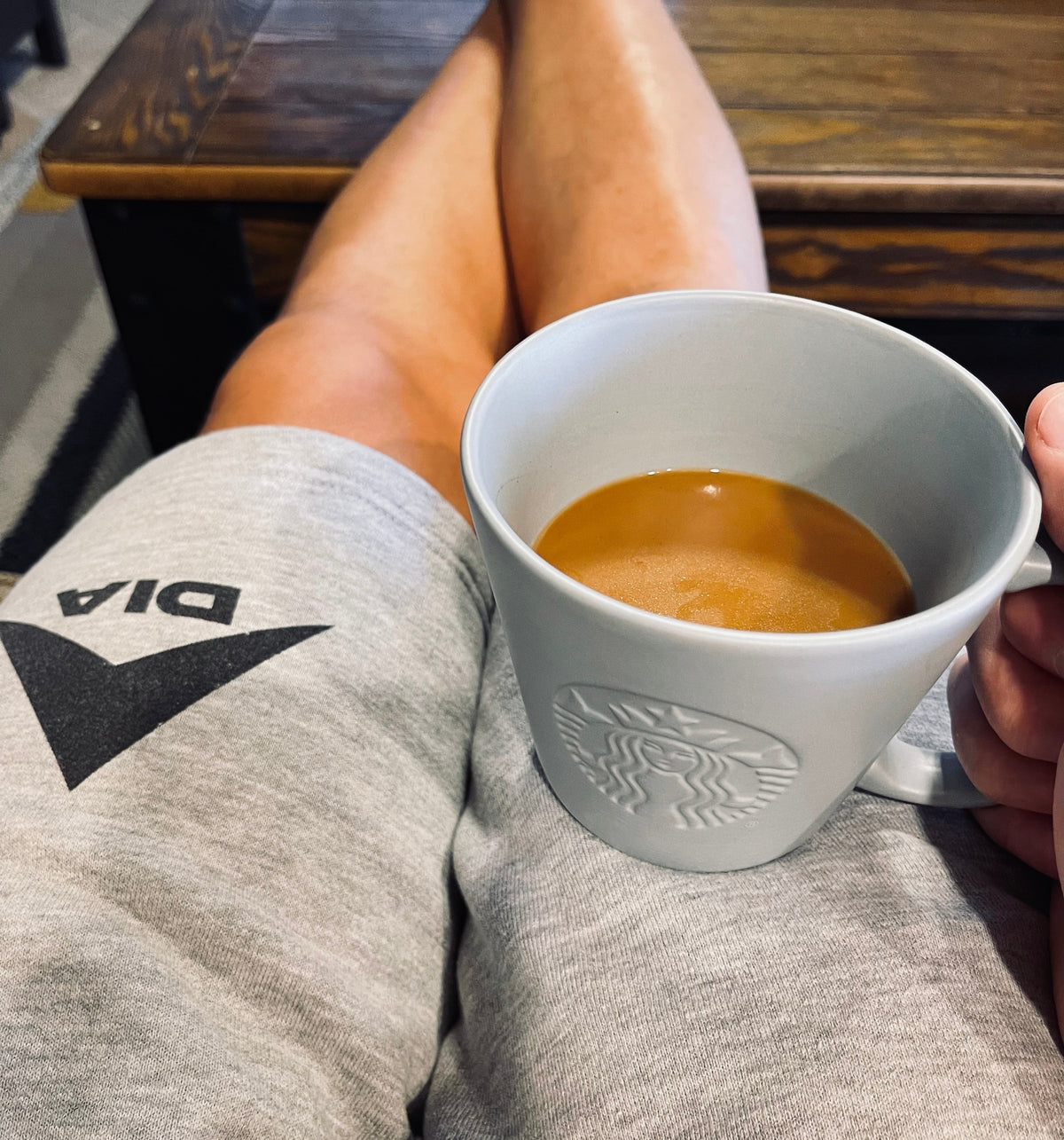 Person with crossed legs, indoor setting with a table, with gray DIA sweatpants and a white Starbucks coffee mug.