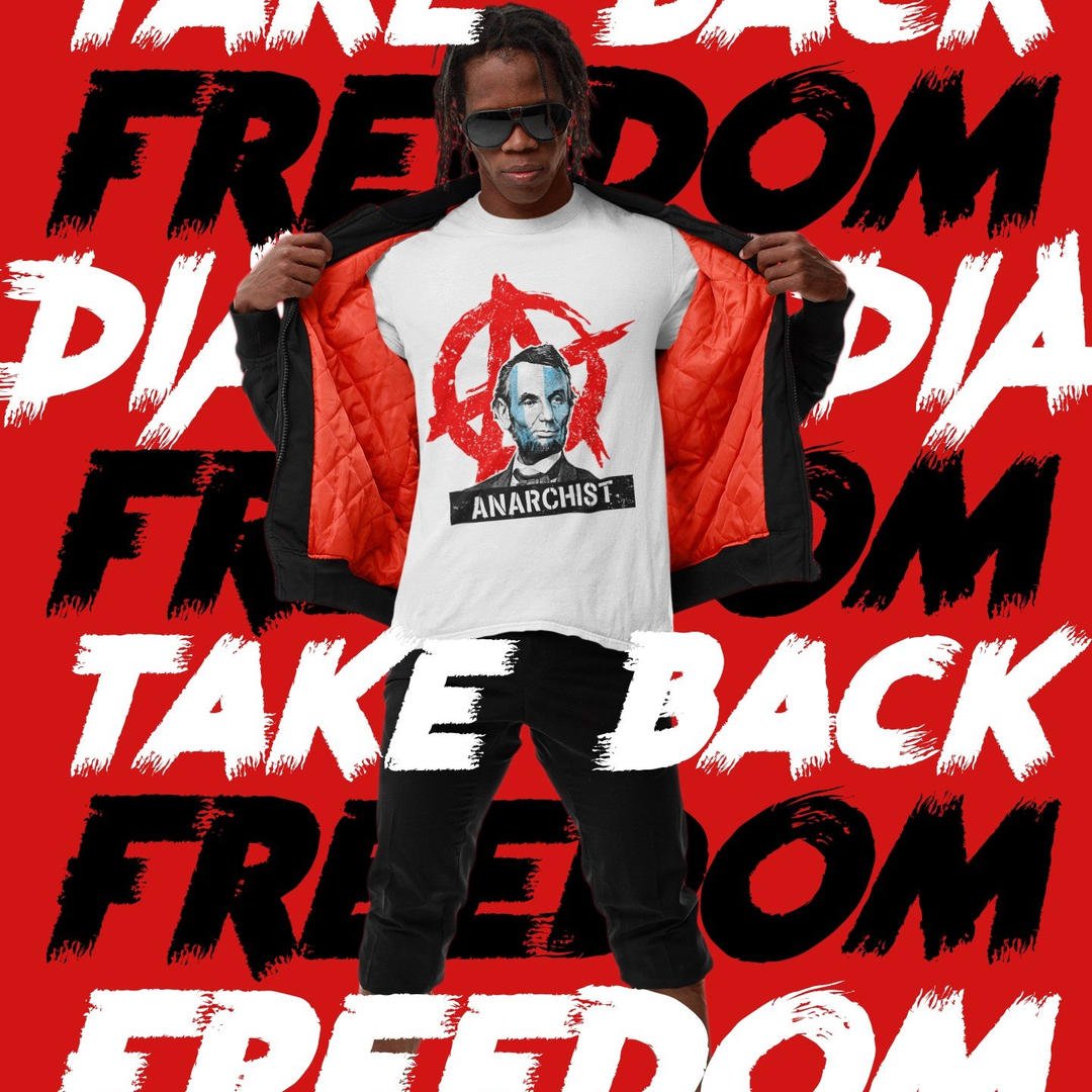 Man in a red-walled setting with "TAKE BACK FREEDOM" text, wearing a white Abraham Lincoln "ANARCHIST" t-shirt.
