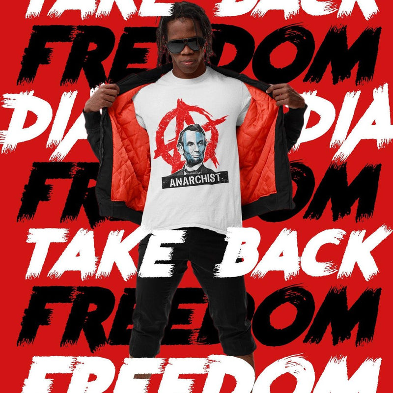 Man in a red-walled setting with "TAKE BACK FREEDOM" text, wearing a white Abraham Lincoln "ANARCHIST" t-shirt.