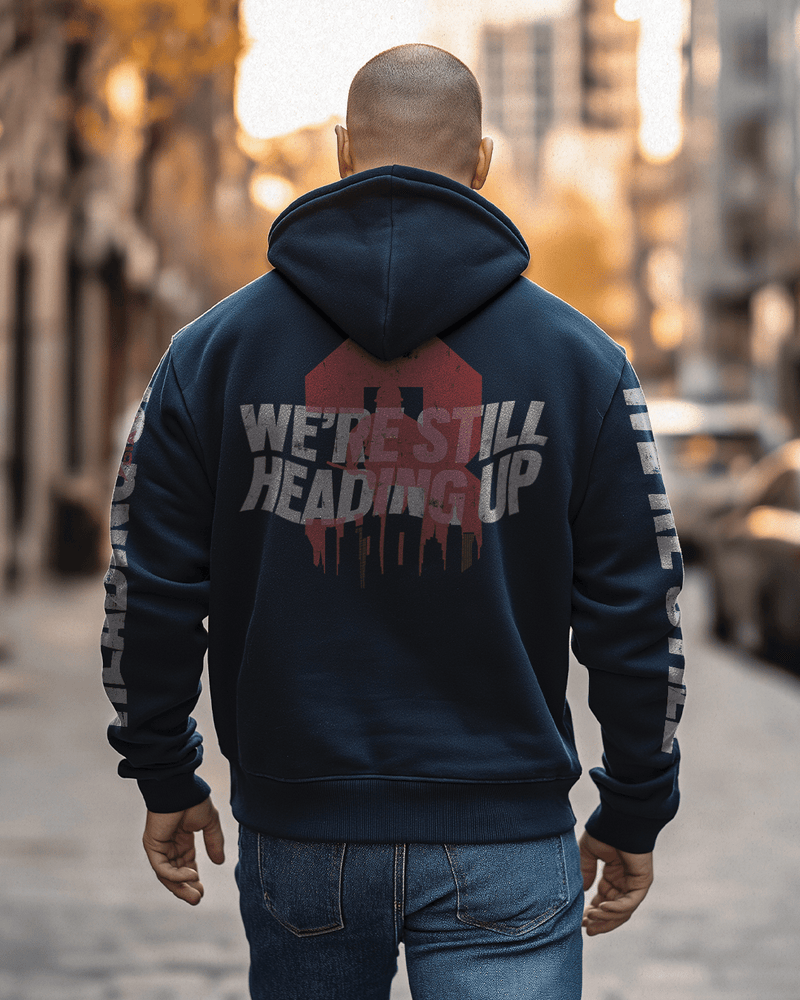 Man walking down a city street, wearing a navy "We're Still Heading Up" hoodie