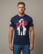 Man in studio wearing navy t-shirt featuring "We're Still Heading Up" firefighter graphic and American flag sleeve patch.