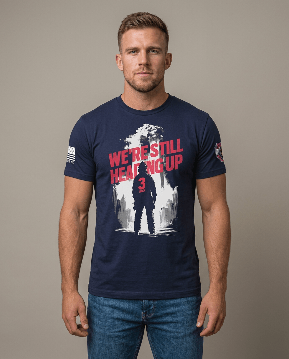 Man in studio wearing navy t-shirt featuring "We're Still Heading Up" firefighter graphic and American flag sleeve patch.