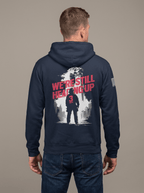 Man from behind in studio wearing navy hoodie with "We're Still Heading Up" back graphic and American flag sleeve patch.