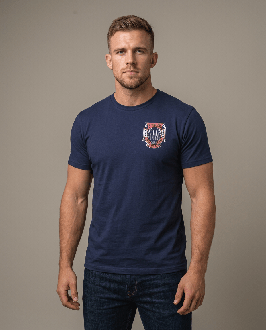 Man in studio wearing a navy T-shirt featuring a 3 Truck 9/11 memorial chest graphic and an American flag sleeve patch.