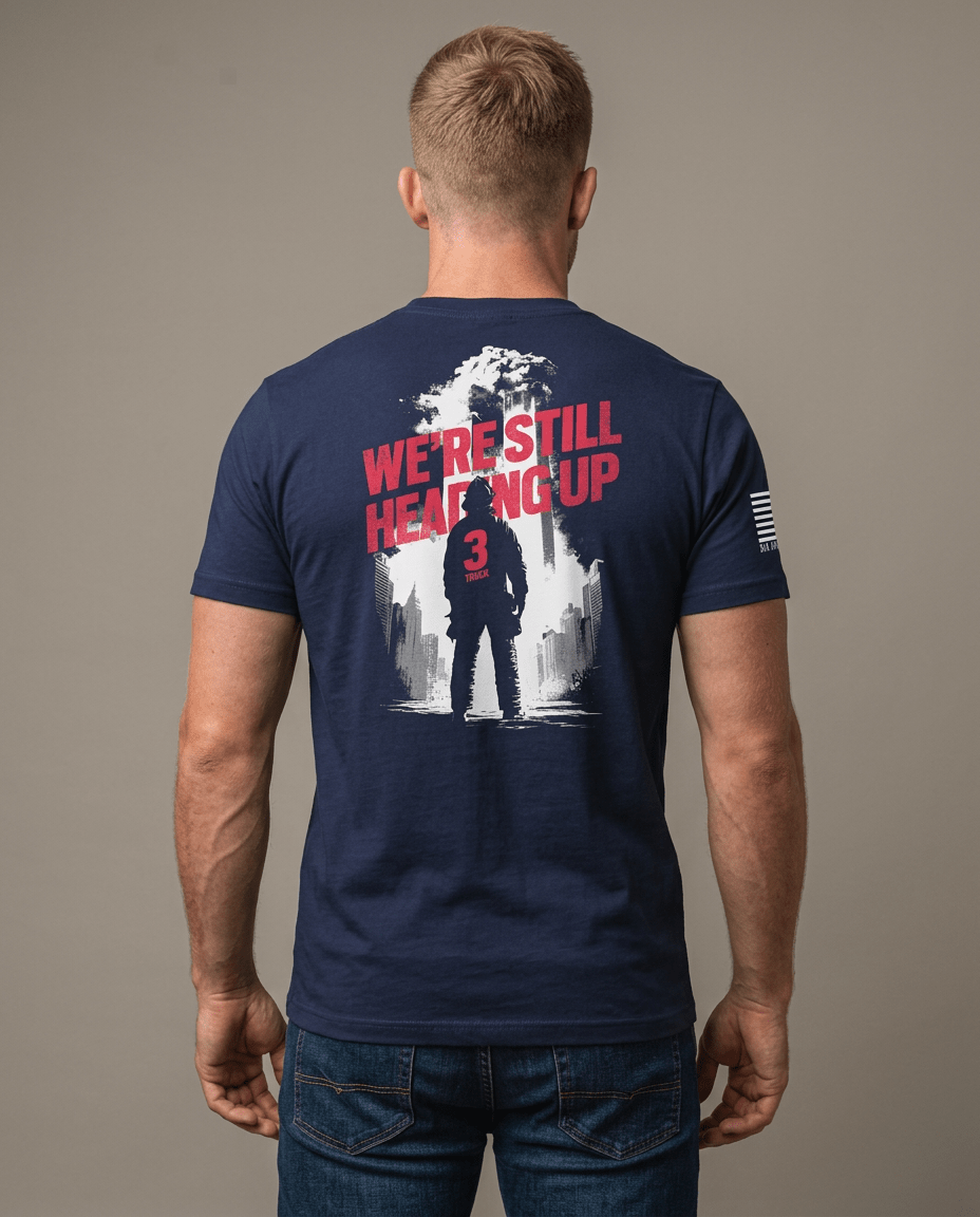 Man from behind in studio wearing navy t-shirt featuring "We're Still Heading Up" firefighter back graphic.
