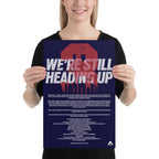 Woman holding a navy blue poster featuring "WE'RE STILL HEADING UP" text, red 3 graphic, and a DIA logo.