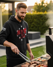 Man wearing a DIA "Chappy" Mako Three Zero Charlie Hoodie grilling burgers and vegetables outdoors, showcasing the hoodie design with stars