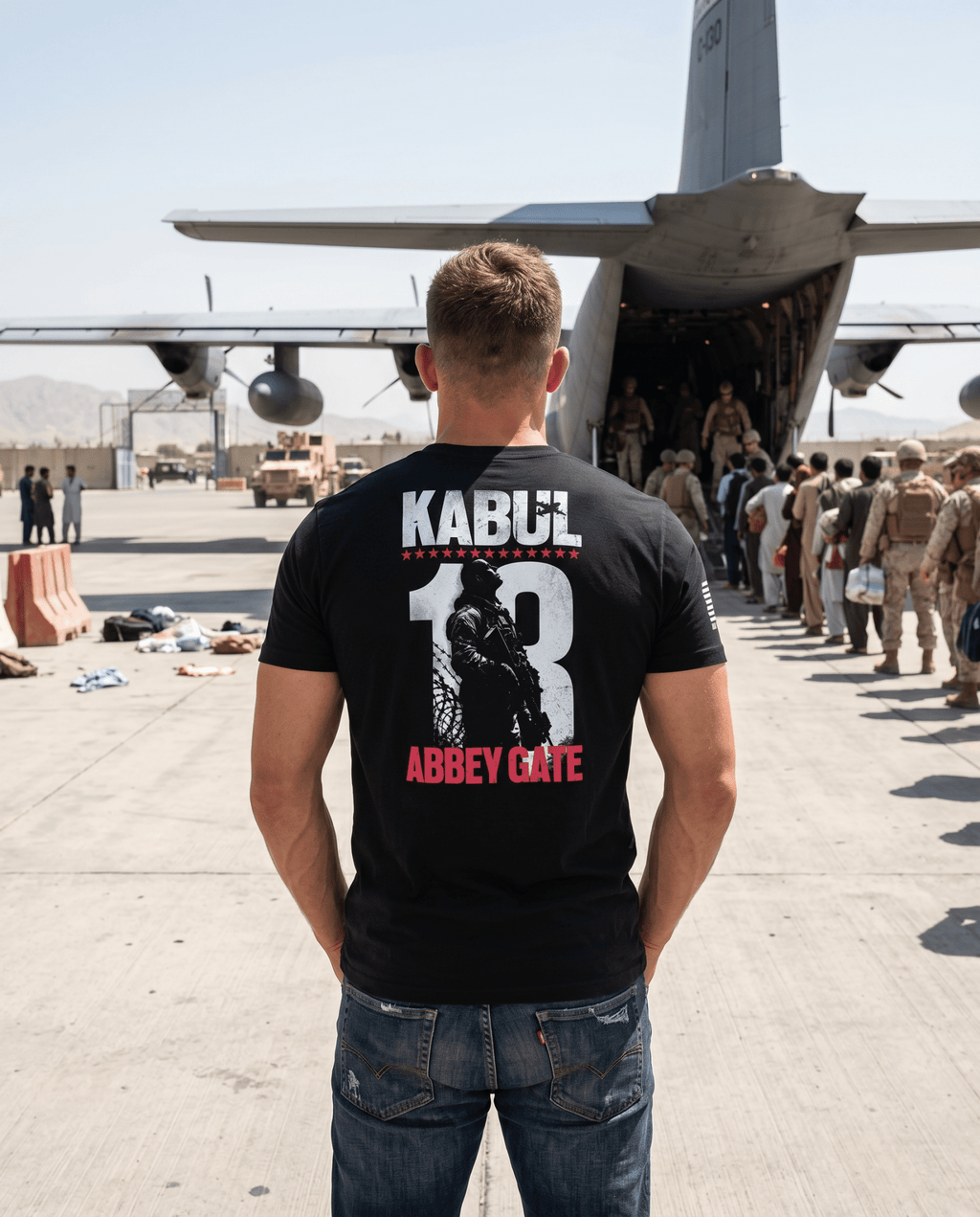 Man on an airfield, black Kabul 13 Abbey Gate graphic t-shirt back view, looking toward a military aircraft.