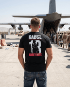 Man on an airfield, black Kabul 13 Abbey Gate graphic t-shirt back view, looking toward a military aircraft.