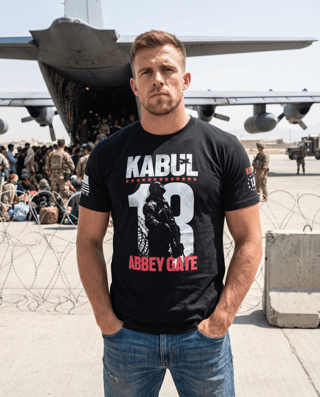 Man on an airfield, black Kabul 13 Abbey Gate shirt, standing close-up, front view with a military aircraft behind.
