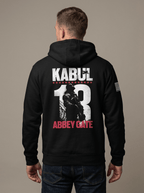 Man from behind in studio wearing black hoodie with Kabul 13 Abbey Gate back graphic and American flag sleeve patch.