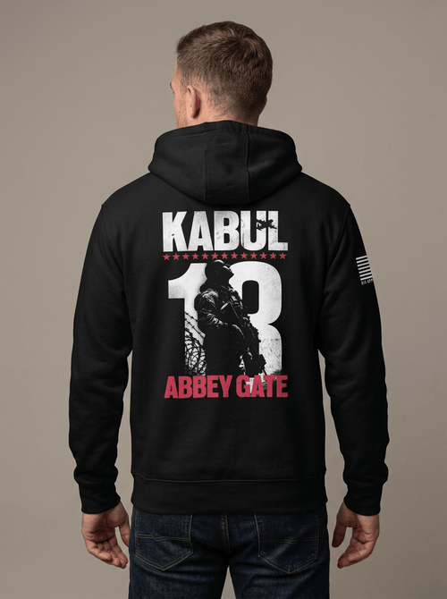 Man from behind in studio wearing black hoodie with Kabul 13 Abbey Gate back graphic and American flag sleeve patch.