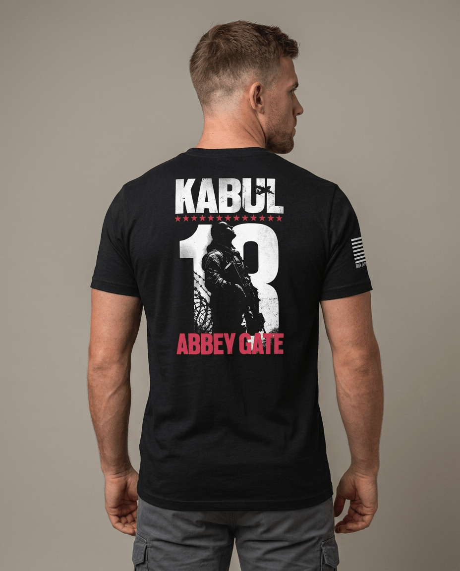 Man from behind in studio wearing black t-shirt featuring Kabul 13 Abbey Gate back graphic and American flag sleeve patch.