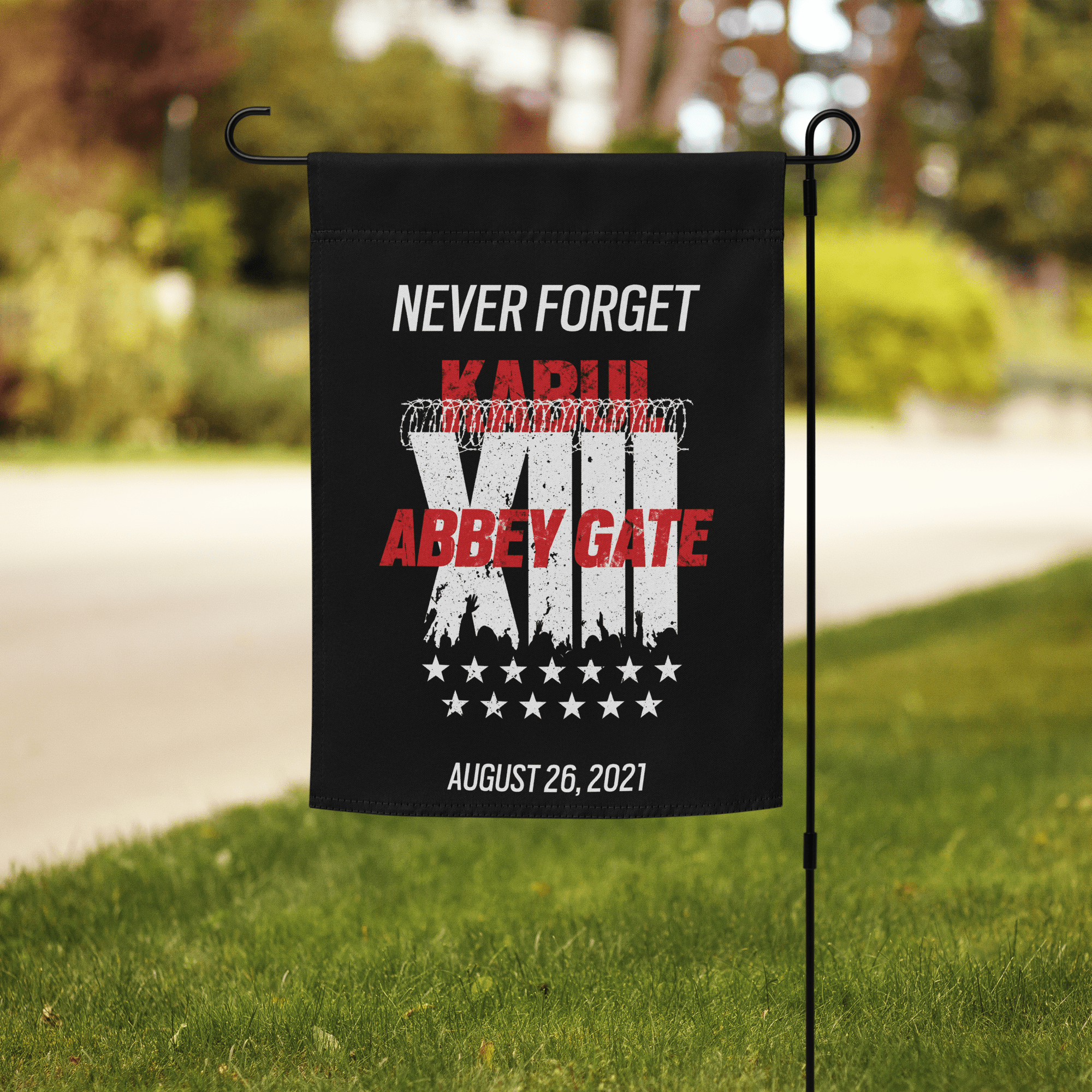 Black garden flag on a lawn with barbed wire, XIII roman numeral, 13 stars, "KABUL", "ABBEY GATE", and "AUGUST 26, 2021".