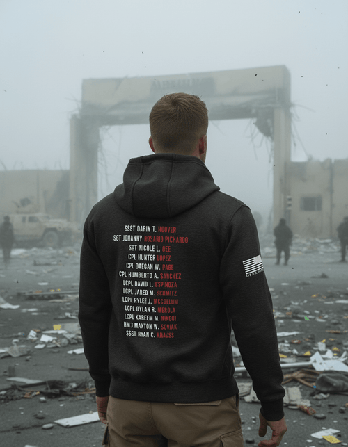 Man standing in debris with a black hoodie back featuring Abbey Gate names and an American flag.