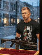 Man with blonde hair by a snowy window wearing a black M203 Christmas t-shirt behind a rifle on a red stand.