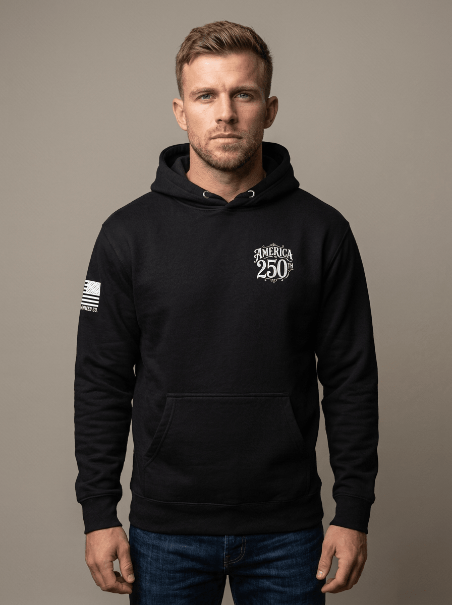 Man in studio wearing black hoodie featuring "AMERICA 250TH" chest graphic and American flag sleeve patch.
