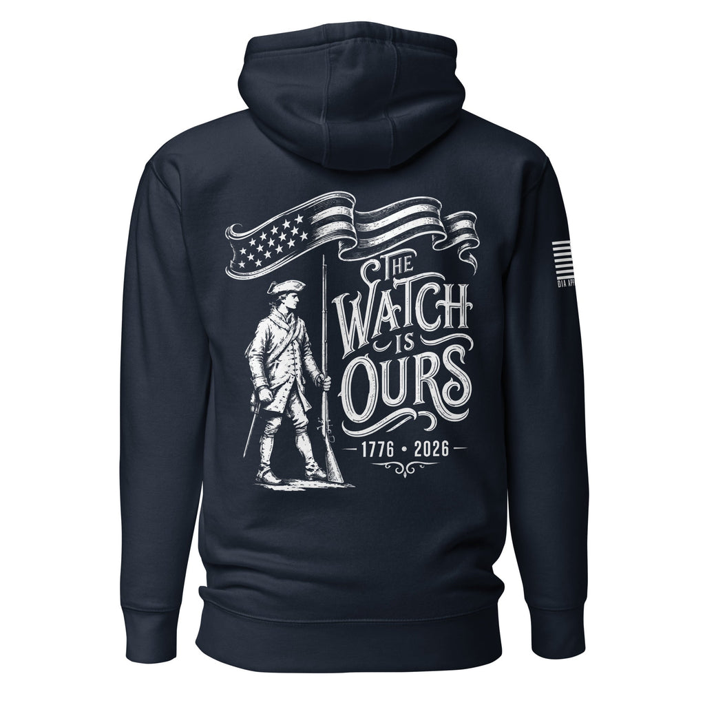 Navy hoodie with "THE WATCH IS OURS 1776-2026" minuteman back graphic and American flag sleeve patch.