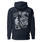 Navy hoodie with "THE WATCH IS OURS 1776-2026" minuteman back graphic and American flag sleeve patch.
