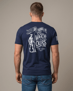 Man from behind in studio wearing navy t-shirt with "THE WATCH IS OURS 1776-2026" minuteman back graphic.
