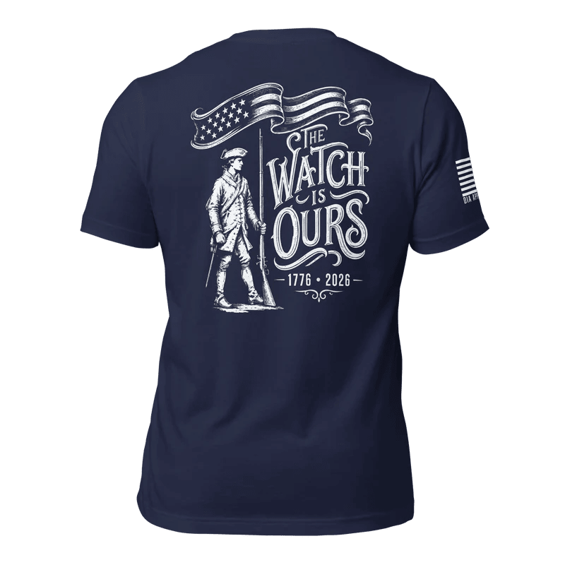 Navy t-shirt with "THE WATCH IS OURS 1776-2026" minuteman back graphic and American flag sleeve patch.