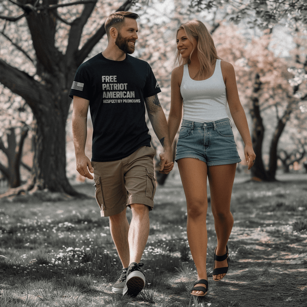 Man and woman walk through a park, he wears a black American Pronouns DIA shirt.