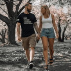 Man and woman walk through a park, he wears a black American Pronouns DIA shirt.