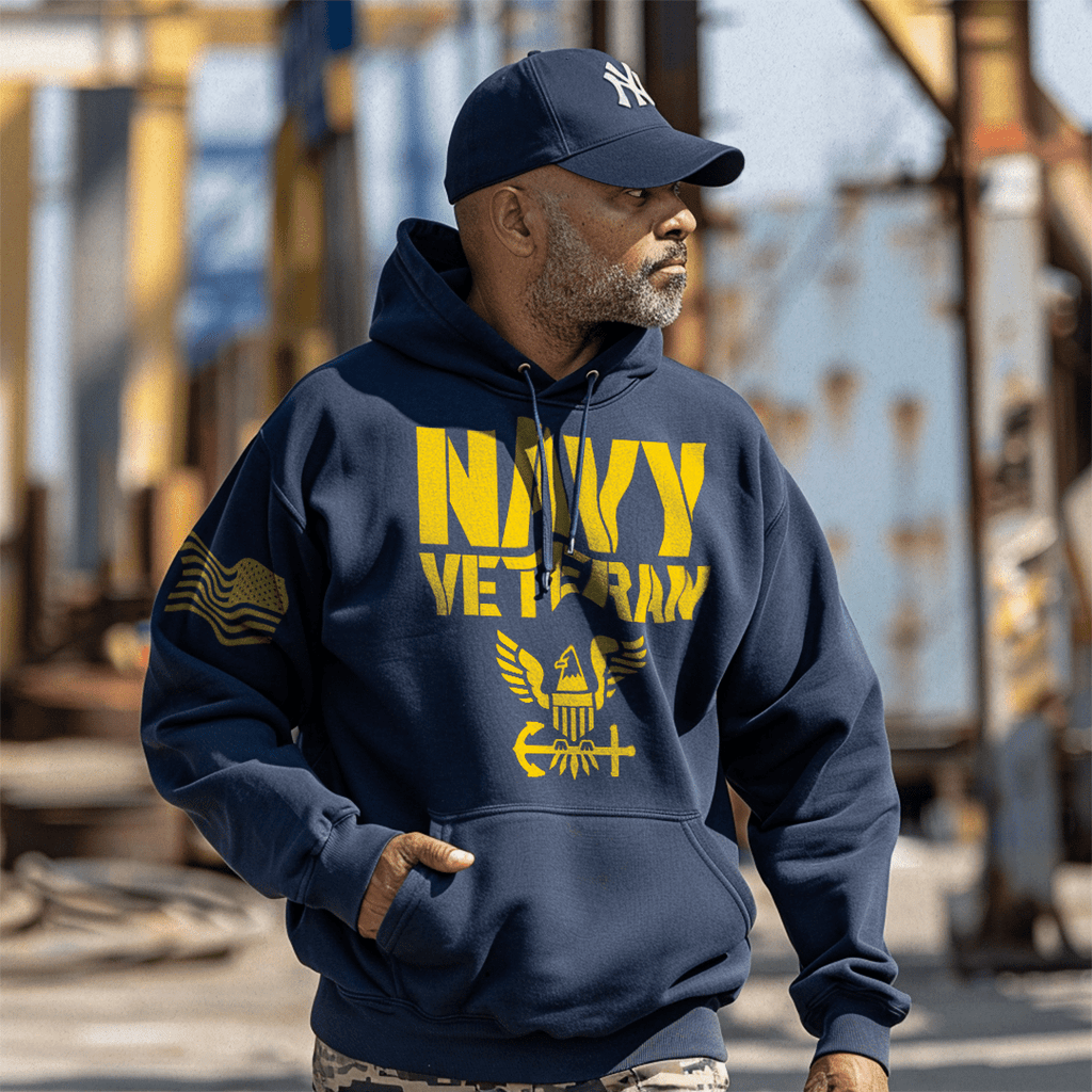 A man wearing a navy blue hoodie featuring "NAVY VETERAN" text and a Navy emblem, stands in an industrial setting.