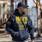A man wearing a navy blue hoodie featuring "NAVY VETERAN" text and a Navy emblem, stands in an industrial setting.