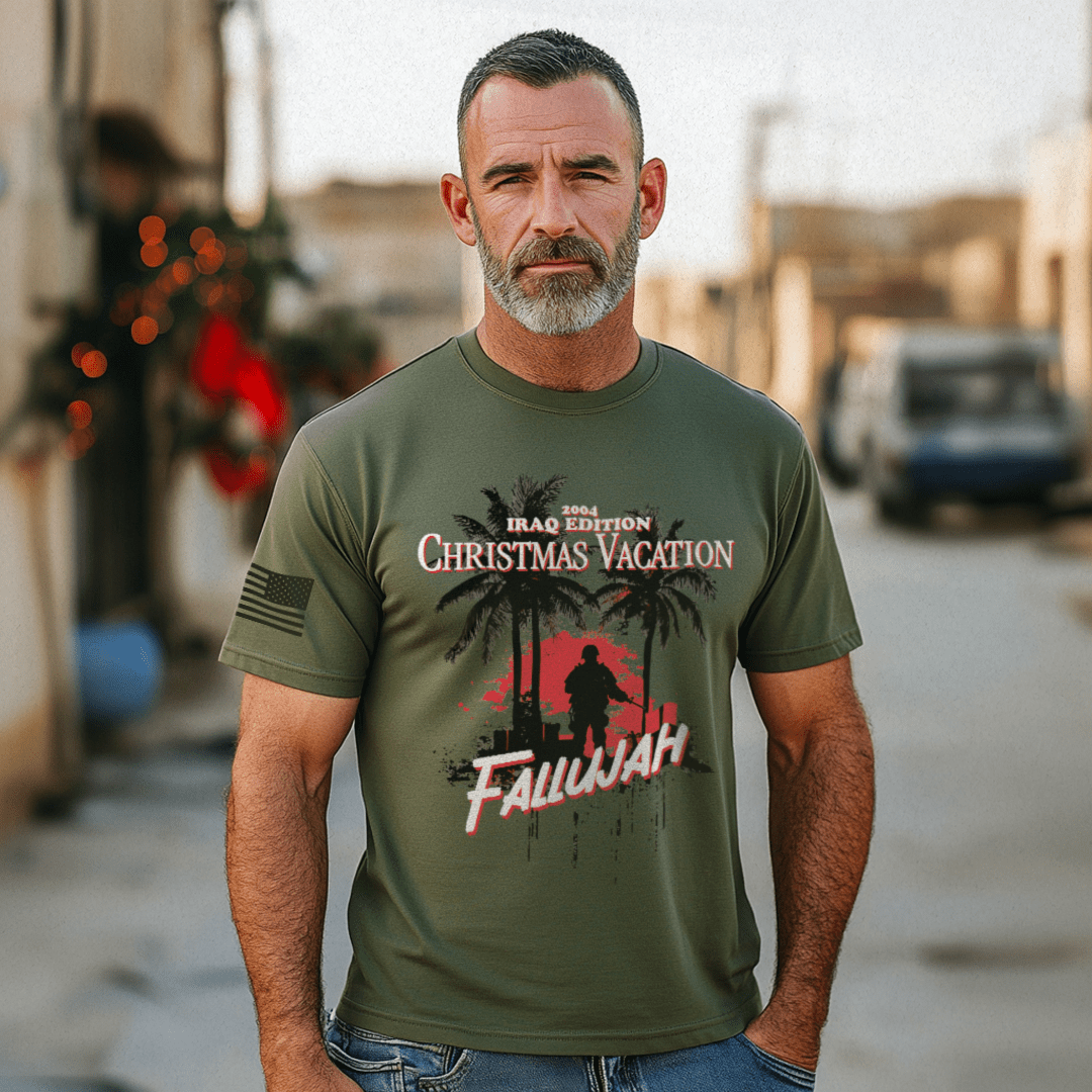 Man with a graying beard outdoors in a sunlit urban area wearing an army green Iraq 2004 Christmas t-shirt.