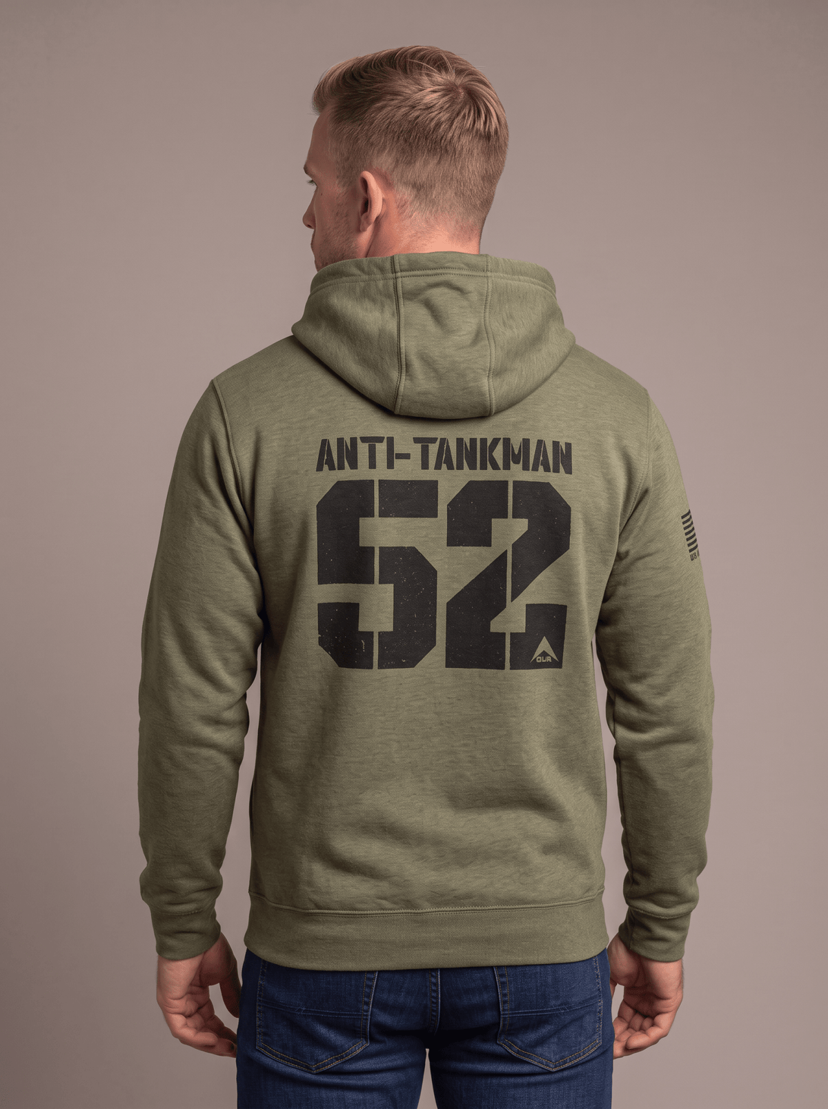 Man stands in studio facing away, wearing green hoodie with "ANTI-TANKMAN 52", DIA logo, and American flag patch.
