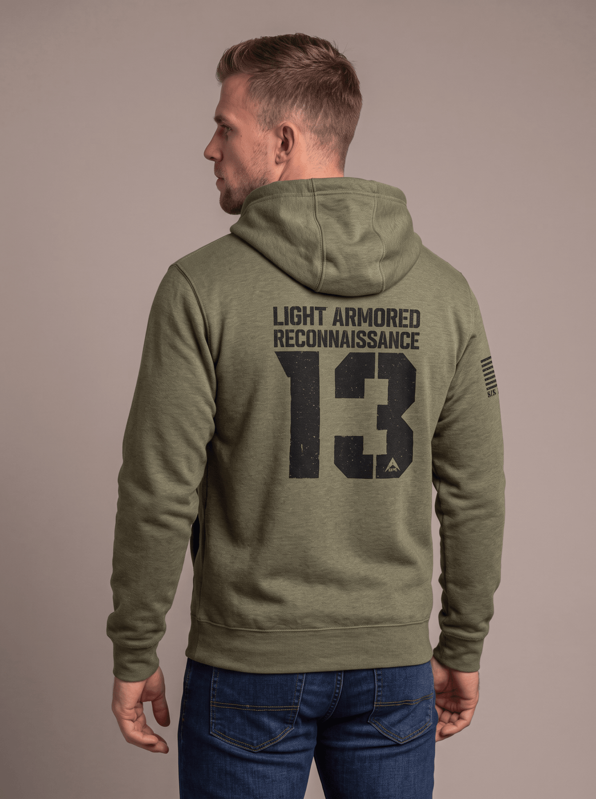 Man in studio facing away, wearing green hoodie with "LIGHT ARMORED RECONNAISSANCE 13", DIA logo, American flag patch.