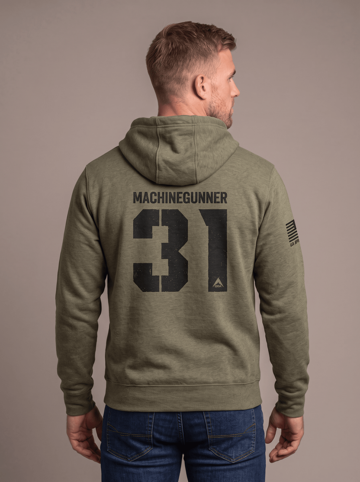 Man stands in a studio facing away, wearing a green hoodie with "MACHINEGUNNER 31", DIA logo, and an American flag patch.