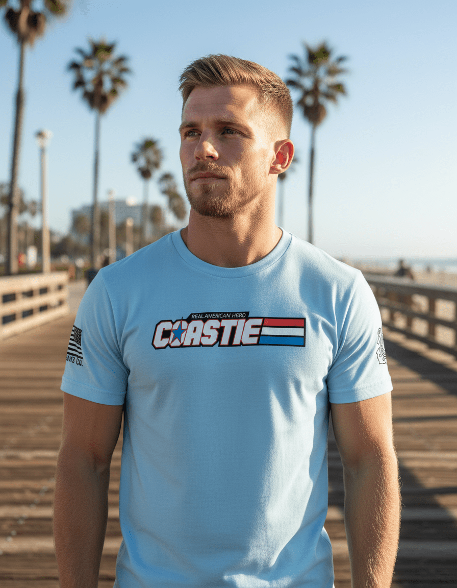 A man stands on a sunny boardwalk with palm trees wearing a light blue "COASTIE" t-shirt and American flag.