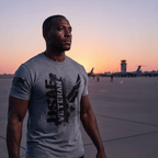 A man stands on an airfield at sunset, wearing a gray "USAF VETERAN" t-shirt with an American flag on the sleeve.