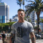A tattooed man walks through a city setting wearing a gray "USCG VETERAN" t-shirt with a DIA logo on the sleeve.