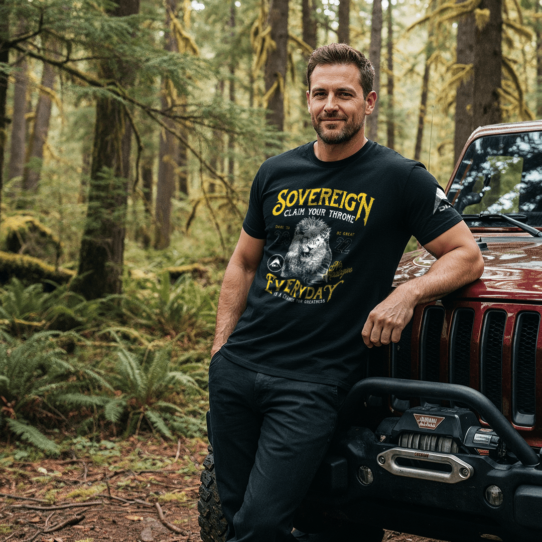 A man leans against a red Jeep in a lush forest wearing a black "SOVEREIGN" lion graphic t-shirt and dark pants.