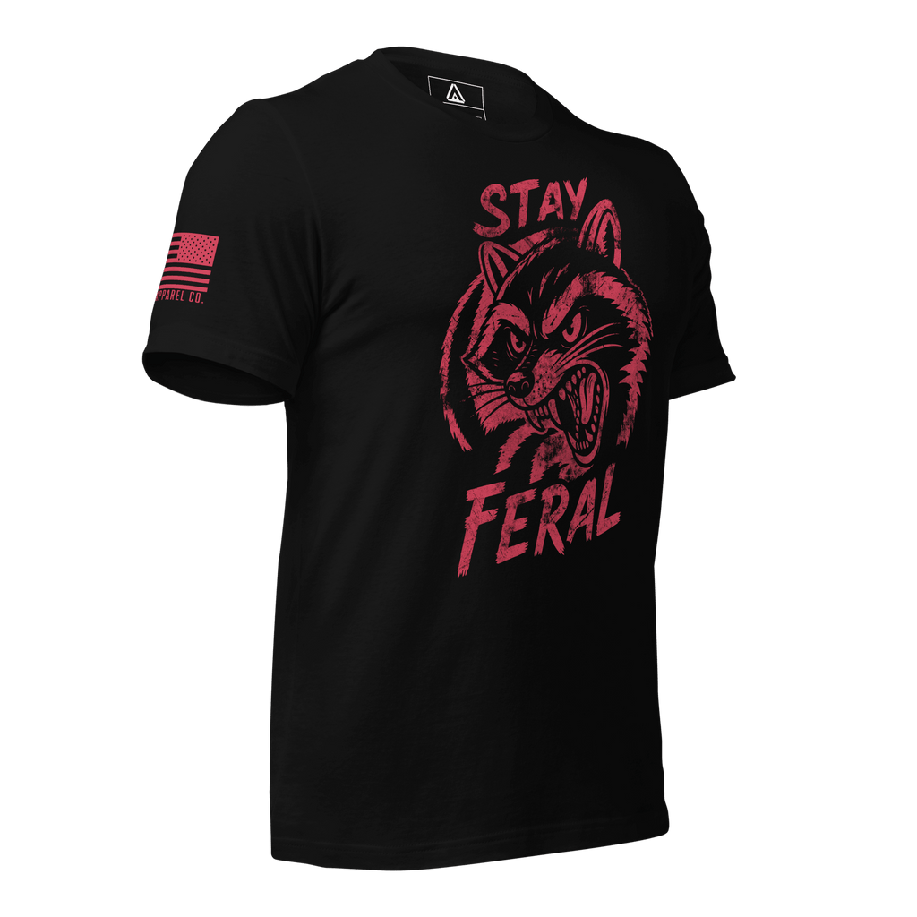 Black t-shirt shown angled right, with red "Stay Feral" snarling raccoon graphic and red American flag on right sleeve.