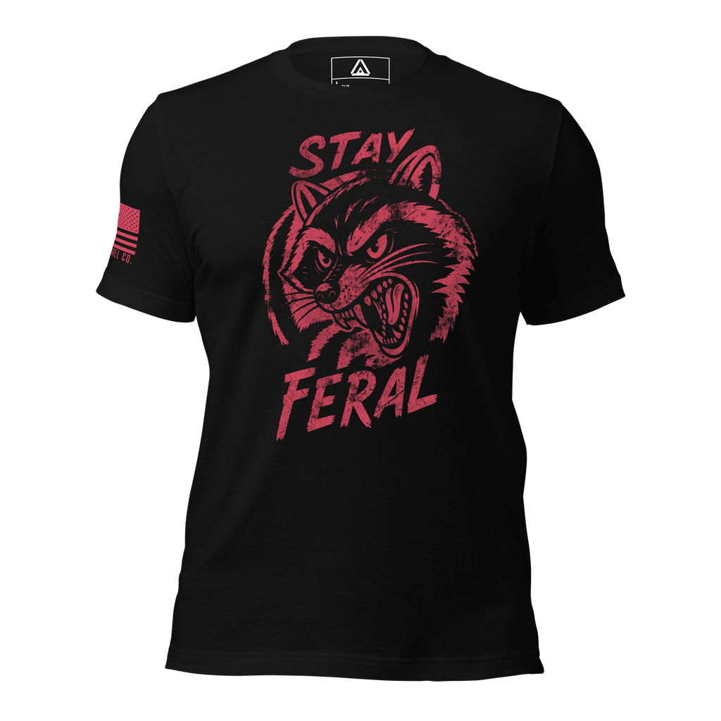 Black t-shirt with distressed red "Stay Feral" snarling raccoon graphic and an American flag patch on right sleeve.