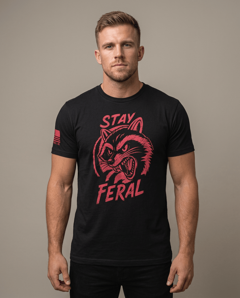 Man in studio wearing a black t-shirt with a red "STAY FERAL" snarling raccoon graphic and an American flag sleeve patch.