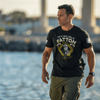 A man near water wearing a black "INVINCIBLE PATTON" t-shirt with a George Patton graphic and white star on the left sleeve