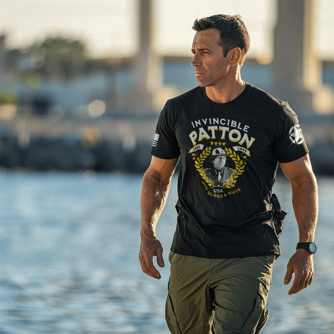A man near water wearing a black "INVINCIBLE PATTON" t-shirt with a George Patton graphic and white star on the left sleeve