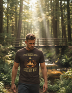A man in a forest setting, wearing a brown t-shirt with the text "LET THE BRIDGES I BURN LIGHT MY WAY" and a bridge graphic.