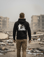 Man in a warzone with rubble wearing a black hoodie with a white soldier graphic with a red stamp and a white American flag.
