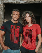 Man and woman in front of a stone building, wearing black and red "RED" t-shirts with DIA logo on the sleeves.